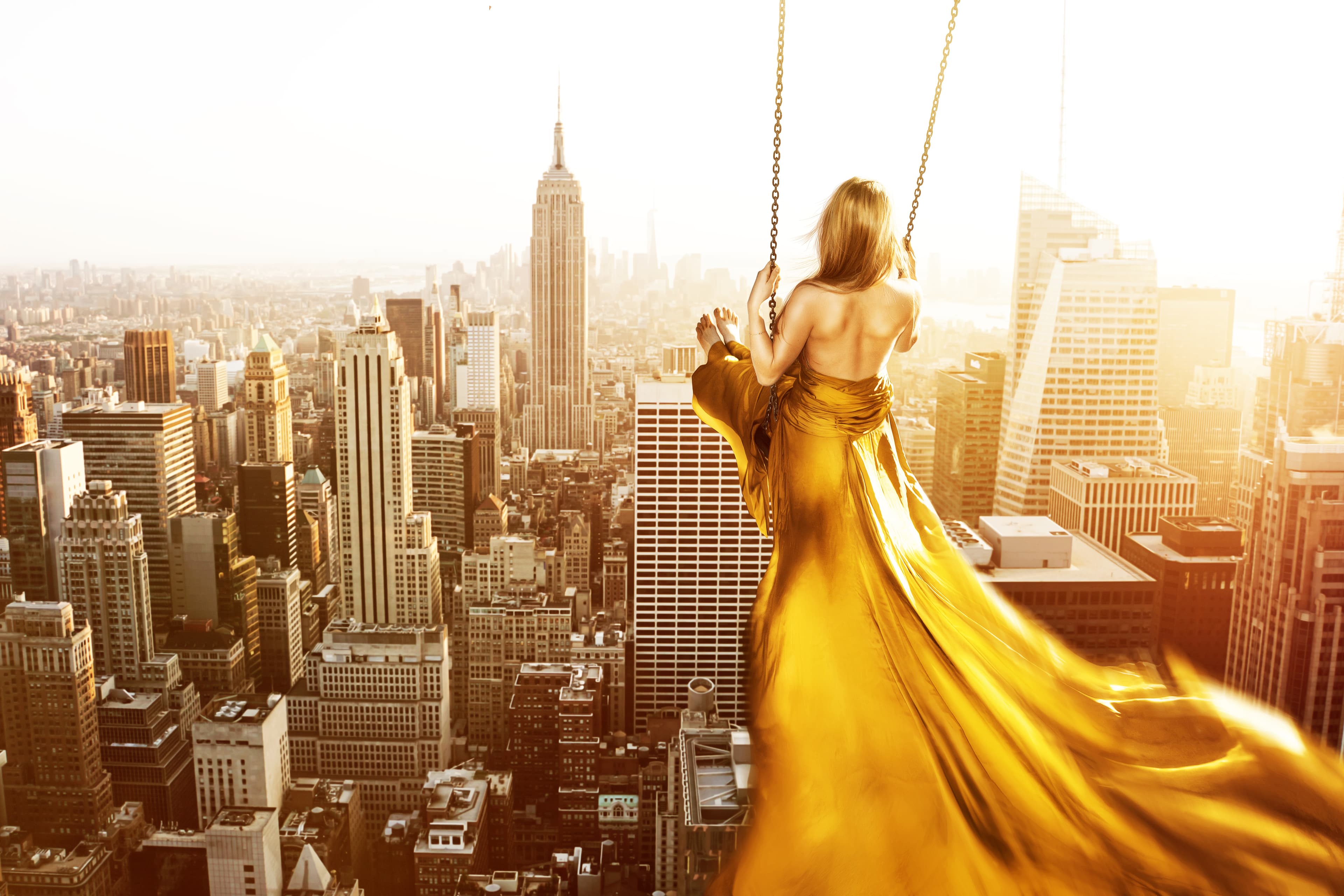 A woman in a golden dress sits on a swing and swings over the rooftops of Vienna